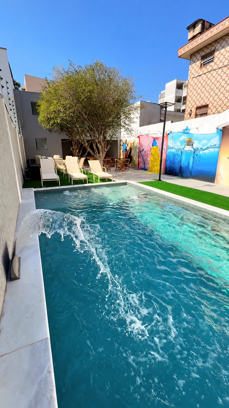 Piscina do Espaço Ecovilla com espreguiçadeiras, árvore e mural colorido